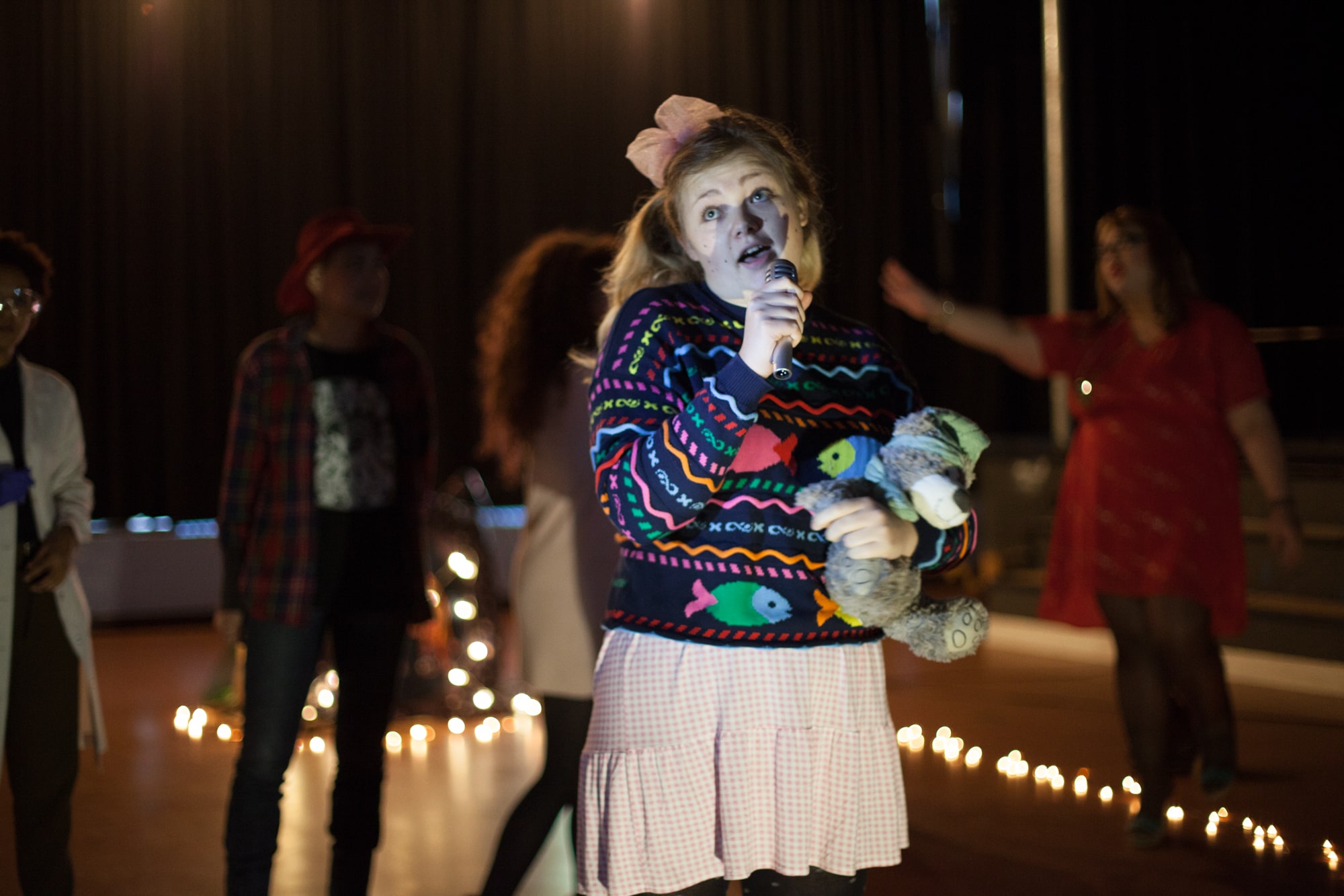Act Attack theatre class performing girl in her 20s blonde hair dressed like a baby girl holding microphone