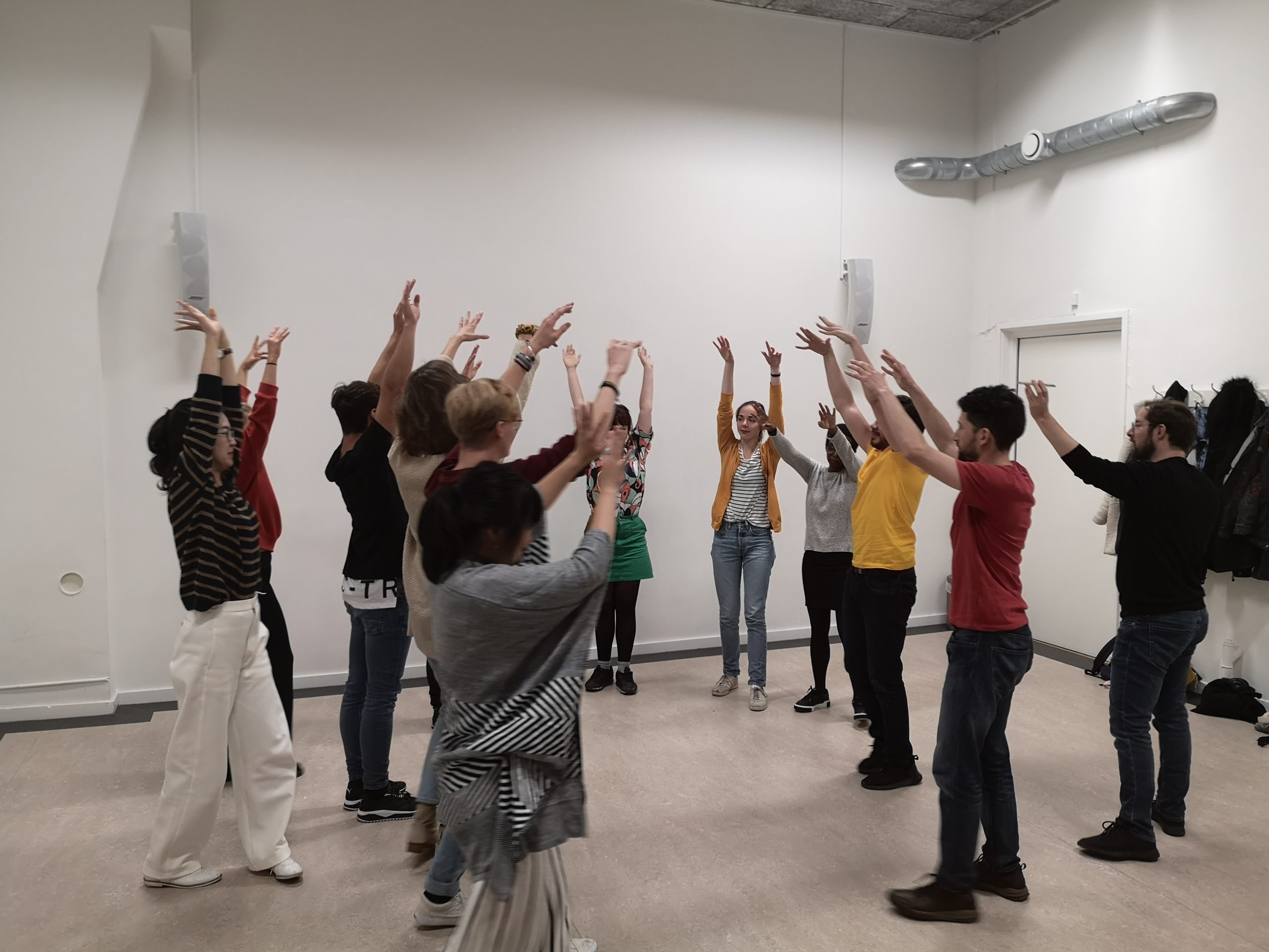 Pure improv for beginners. A group of people form a semi-circle holding their hands up in the air.