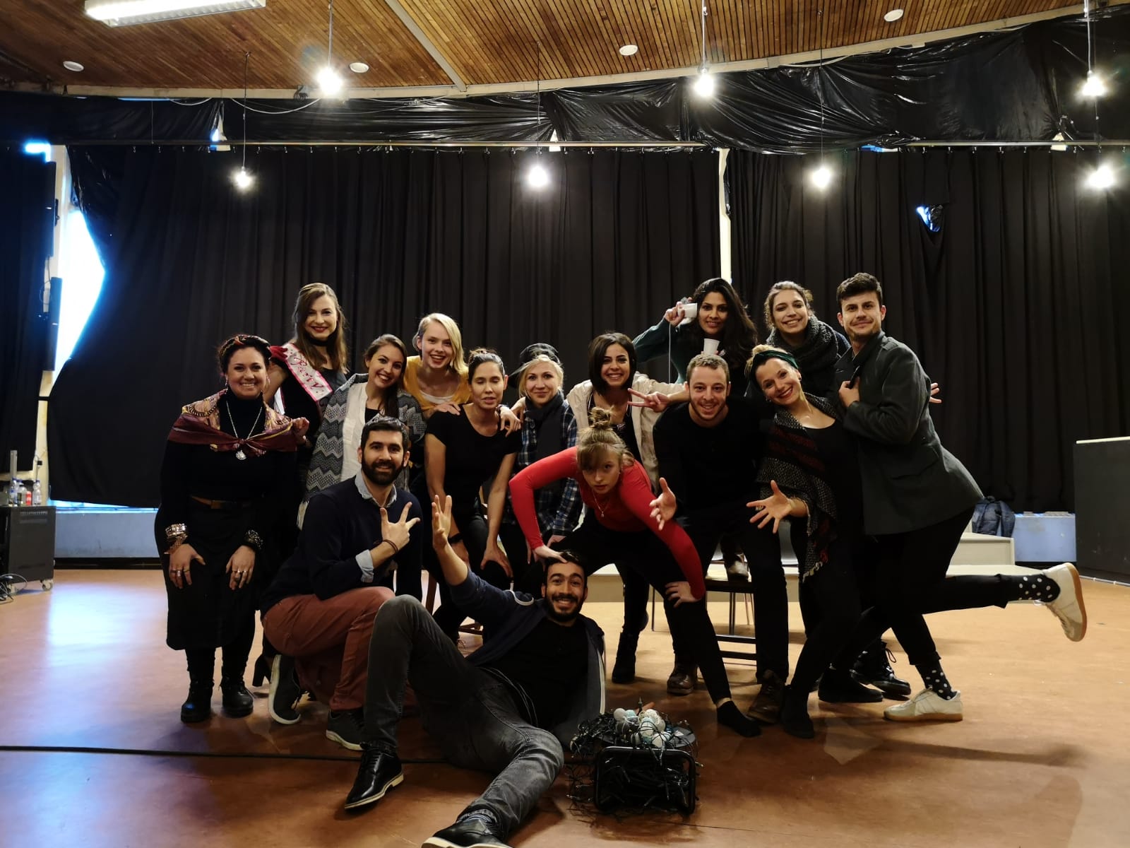 Photo from the show "The Skin of our Teeth". A group of people pose for the picture. Most of them wear black. At the back, there is a black curtain
