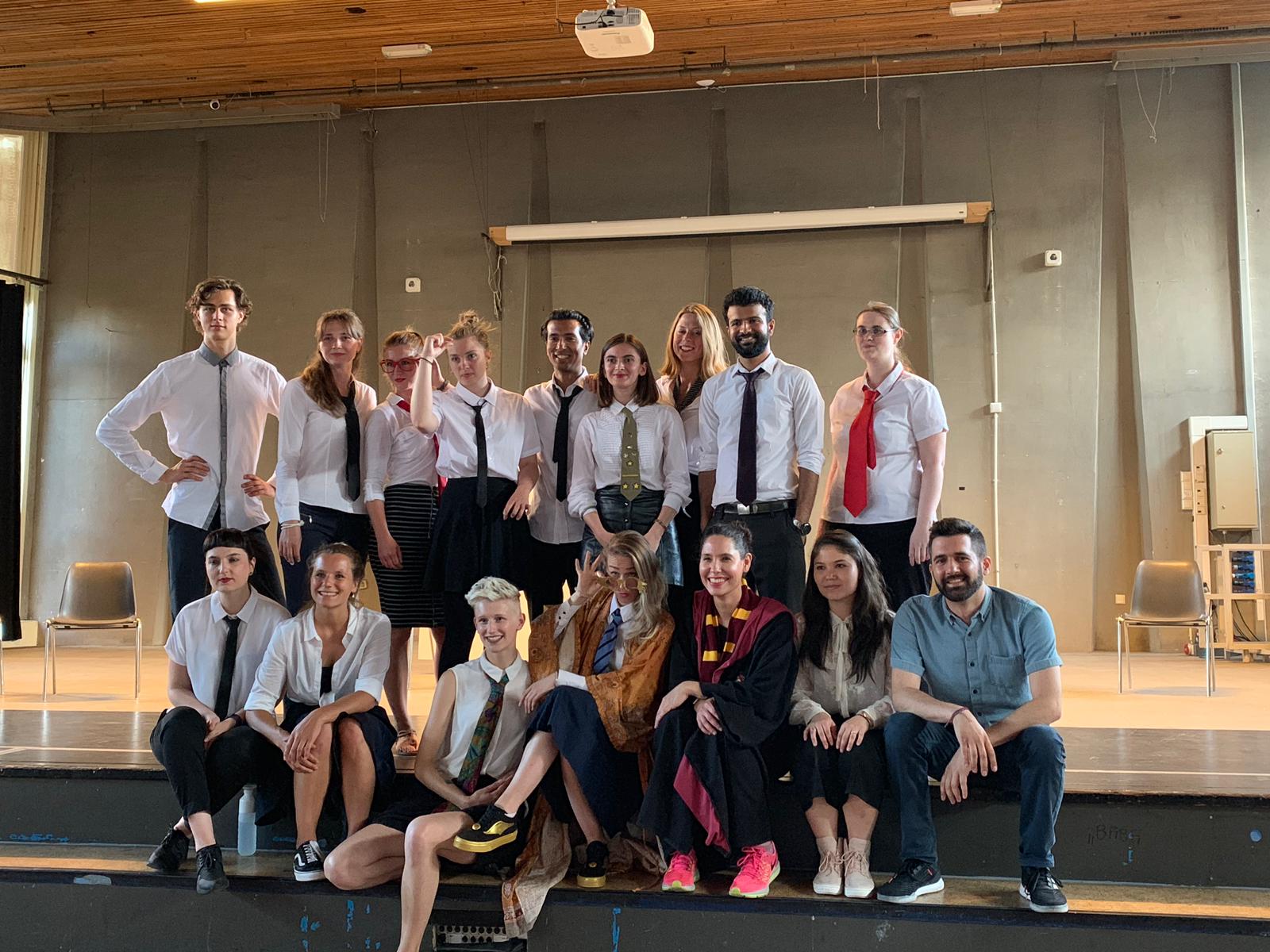 Photo from the rehearsal of the show "the magic school". A group of people pose for the picture. Most of them wear a white shirt and tie