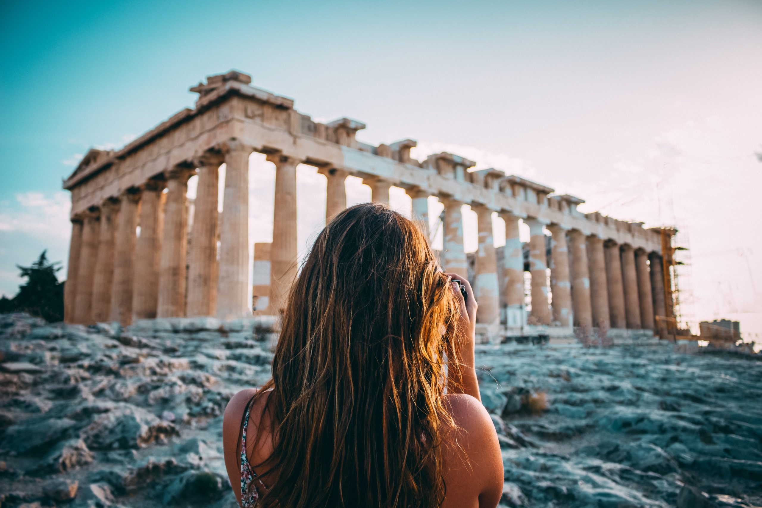 Backside of a woman with brown hair who is taking a picture of the temple of Parthenon