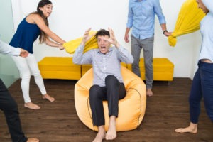 Four playful business people beating their friend with pillows. He is sitting on beanbag and pretending to be scared.