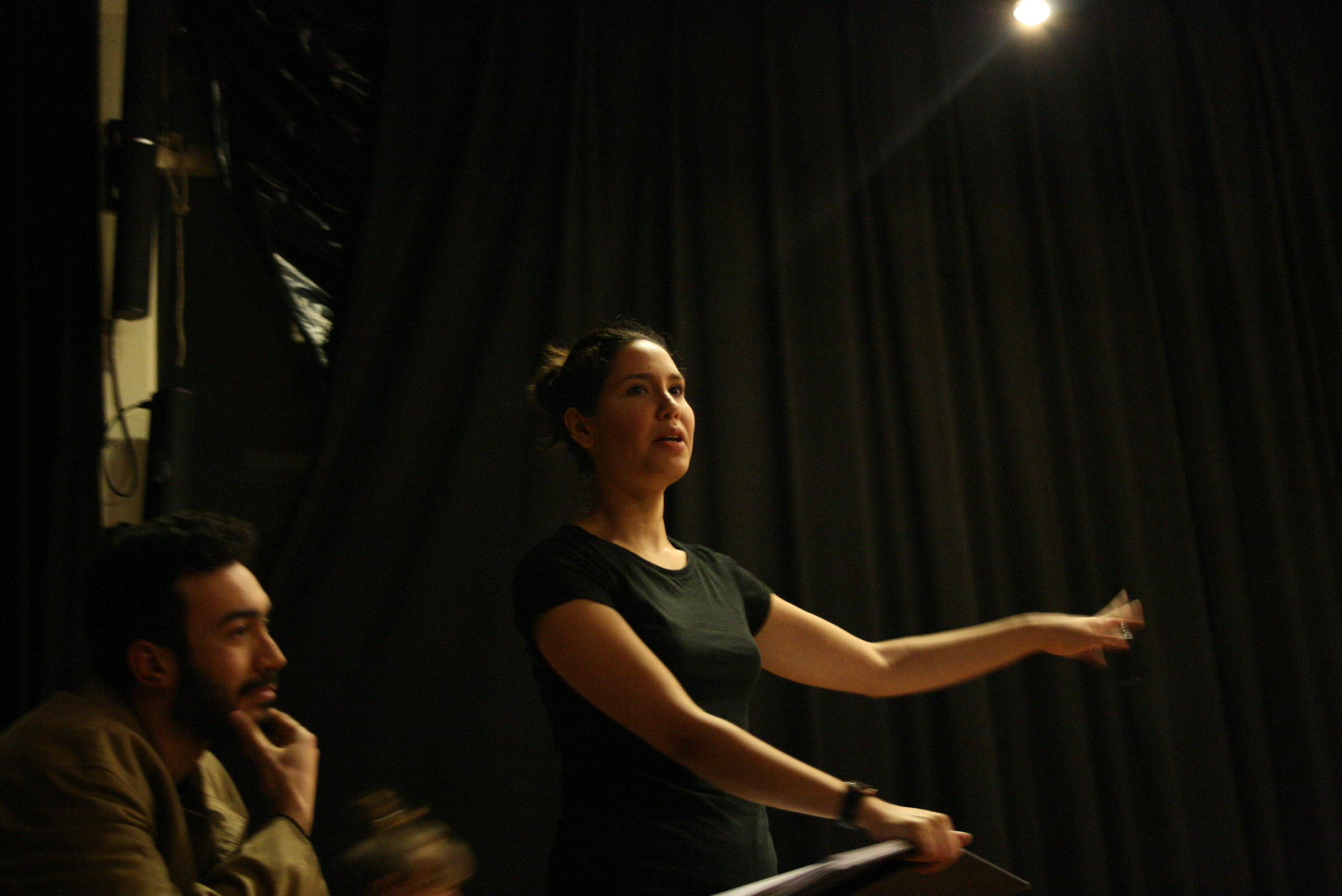 Photo from the show "Skin of our Teeth". A female actor, probably backstage, waves at someone. At the left of the photo, behind her, a man, touching his chin.
