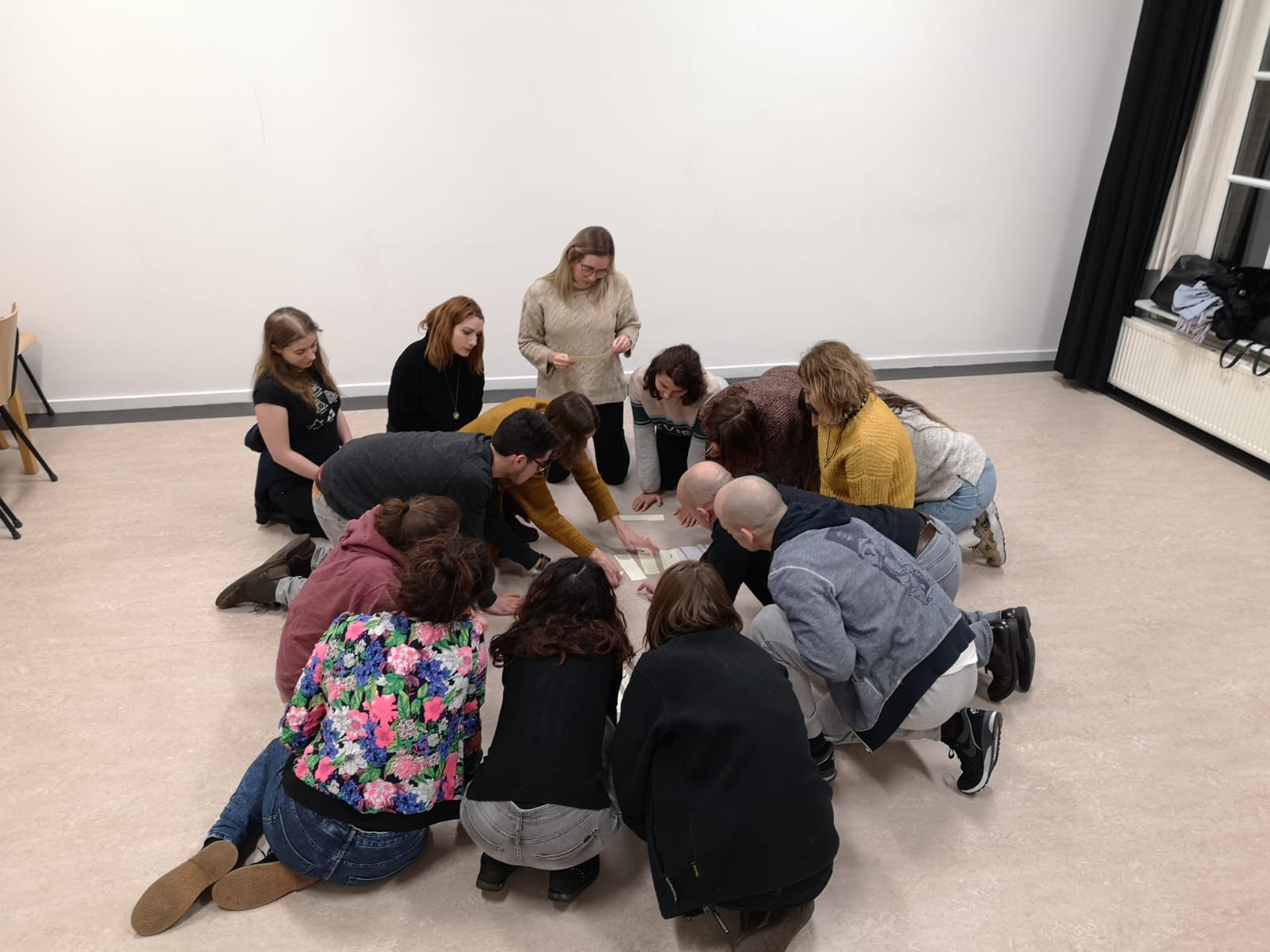 Acting Class Act Attack. A group of people form a circle, sitting on the floor, looking at some notes they have laying on the ground
