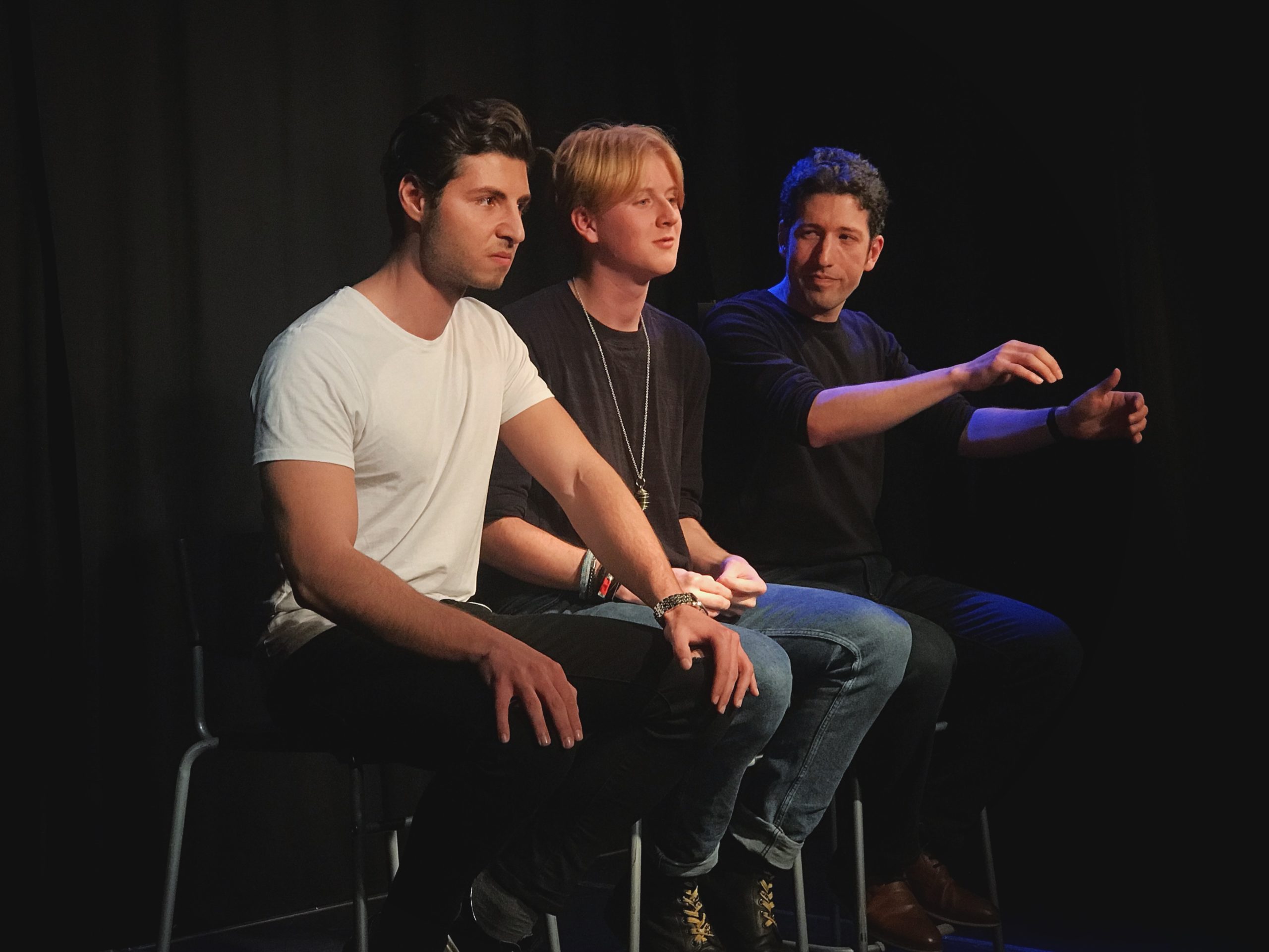 Act Attack's Pure improv show. Three men sit on bar stools. One of them pretends to drive